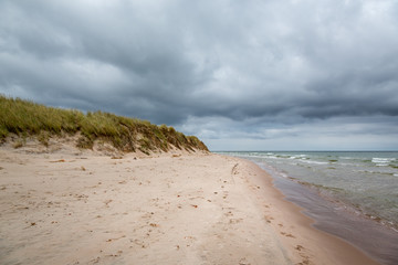 Dark clouds and stormy weather over beautiful island beach with grass and water with waves.