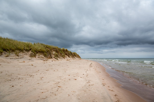 Dark clouds and stormy weather over beautiful island beach with grass and water with waves.