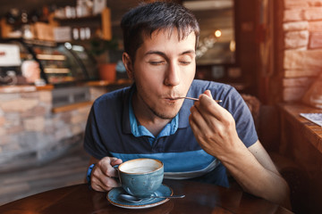 Fototapeta na wymiar Young man enjoying coffee with piece of cake in cafe