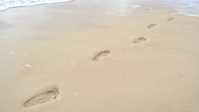 Waves crashing on shore wipe away footprint in the sand on beach