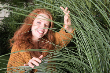 schöne rothaarige Frau zwinkert durch Gräser hindurch