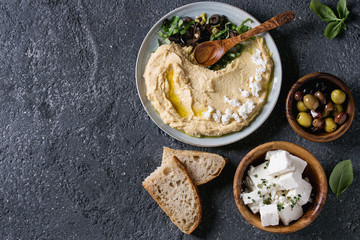Homemade traditional spread hummus with chopping olives and herbs on blue plate, served with bread,...