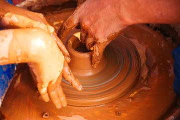 Dirty hands in the clay and the potter's wheel with the product. Father is teaching his dautgher to work with clay.