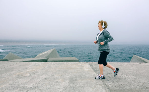 Senior Sportswoman With Headphones Running By Sea Pier