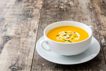 Pumpkin soup in white bowl on wooden table
