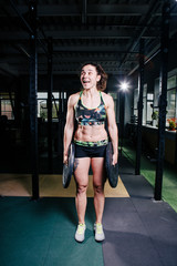 Fototapeta na wymiar Fit power athletic confident young woman crossfit trainer doing exercises with heavy weight barbell plate in gym rising hand. Fitness muscular body, strong hand . Pumping up muscles
