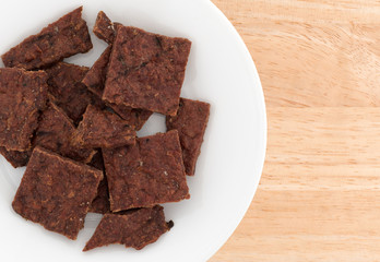 Top close view of peppered beef jerky on a white plate atop a wood table.