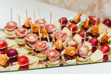 Catering services. Glass tray with snacks with brie, grape, bacon, and shrimps in a restaurant. Snacks before the wedding