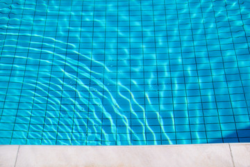 Fototapeta na wymiar Blue ripped water in swimming pool. Swimming pool bottom caustics ripple and flow with waves background. Clear light blue pool water ripples with sun reflections. Surface of blue swimming pool.