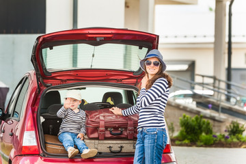 A young woman with a child puts suitcases in the trunk of a red car for travel