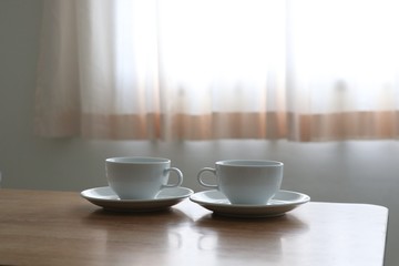 White coffee cups on the wood table near the curtain soft color 