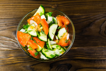 Fresh salad with tomato, cucumber, onion, parsley and dill in glass bowl on wooden table