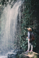 Happy Asian girl standing on stone and waterfall background , concept backpacker in the forest