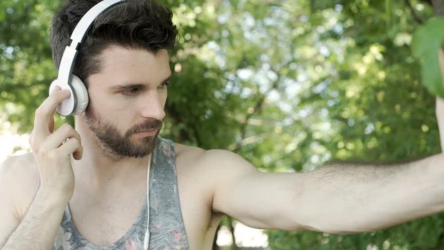 Handsome man in camis shirt listening music on headphones and smiling to the camera, steadycam shot
