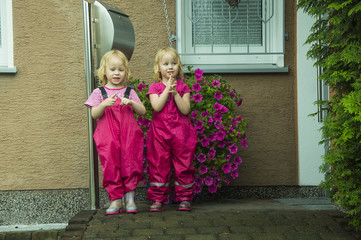 Children, two little girls in pink waterproof suits and rubber boots, stand on the threshold at the...