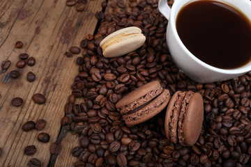 Sweet background of a cup of coffee, coffee beans and cookies macarons on a wooden background. Copyspace on the left.