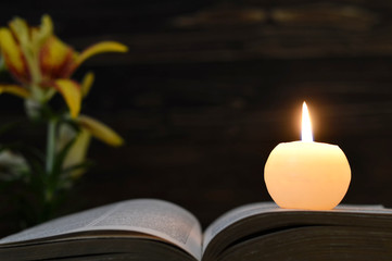 Funeral candle, opened book and flowers on dark wooden background