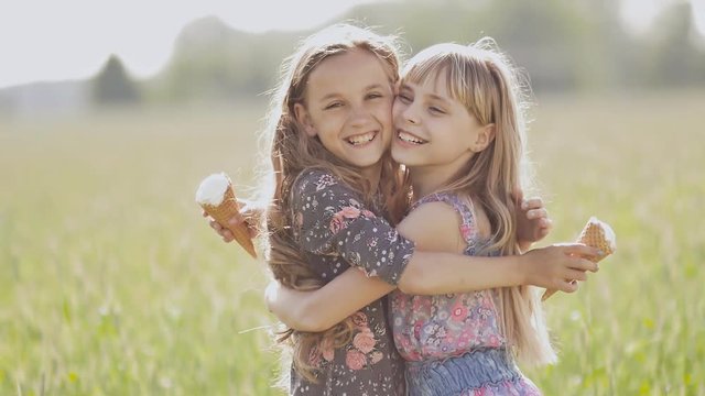 Two little girls sisters posing and hugging holding ice cream in the summer on a sunny day. Two best friends.