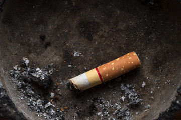Cigarette / Close up of cigarette in dirty ashtray. Dark tone.
