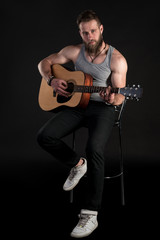 A charismatic man with a beard, playing an acoustic guitar, on a black isolated background. Vertical frame