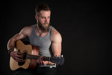 A charismatic man with a beard, playing an acoustic guitar, on a black isolated background. Horizontal frame