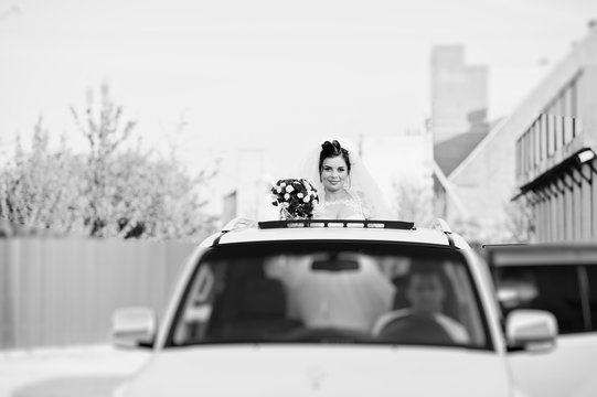 Portrait of a flawless bride looking out of the sunroof in the wedding car. Black and white photo.