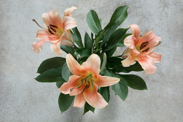 A beautiful bouquet of lilies and green leaves on a vintage background. View from above. Focus on the lilies.
