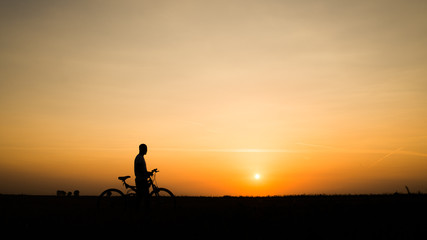 Boy with his bike watching a dramatic sunset