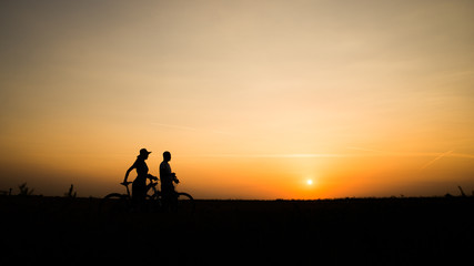 Boy and girl with their bicycles watching a dramatic sunset over a rural field