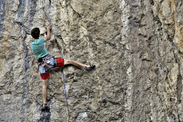 Fototapeta premium Young man climbing on a limestone wall with wide valley on the background