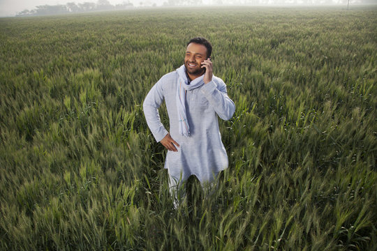 Indian man in a field talking on phone with hand on hip 