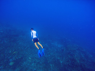 Freediver swims underwater in deep blue sea. Snorkeling man dives up to water surface.