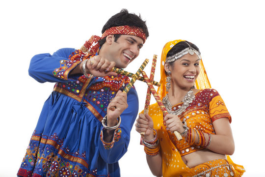 Happy young couple performing Dandiya Raas over white background