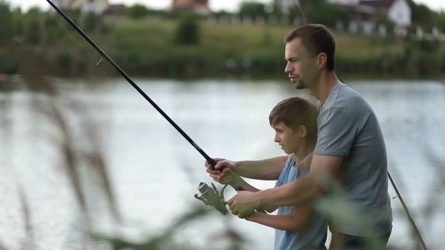 Smiling dad and son fishing and relaxing at pond