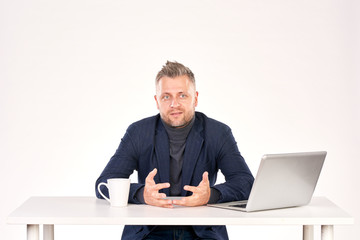 Portrait of middle-aged businessman sitting at office desk with laptop on it