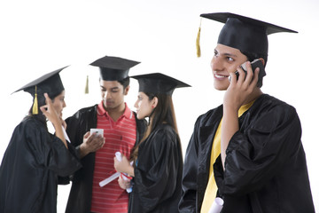 Smiling graduate student answering mobile phone with friends discussing over white background