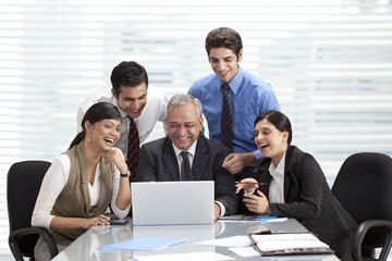 Smiling colleagues at table with laptop 