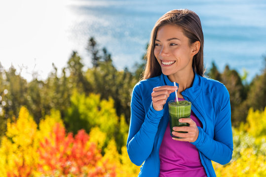 Happy healthy eating girl drinking green smoothie detox outdoors in fall autumn foliage nature retreat. Woman on weight loss diet vegan nutrition cleanse.