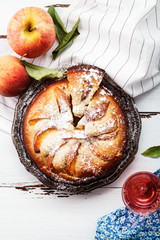 Sweet pie with fresh summer peaches on white wooden distressed background with a glass of rose water. Harvest time concept. Top view