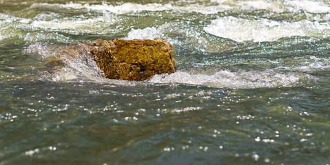 Fast mountain stream splashing and flowing over colorful rock on a bright sunny day
