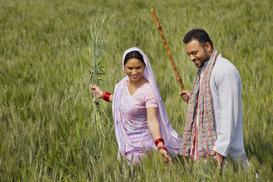 Happy Indian couple gliding through wheat field 