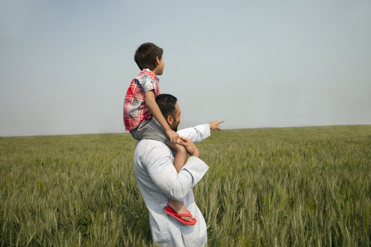 Indian man pointing at something while carrying son on shoulders 