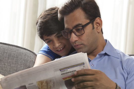 Close-up of father and son reading newspaper 