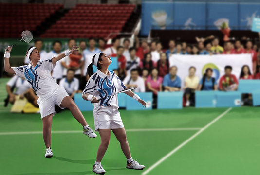 Young female players playing doubles with spectators in the background