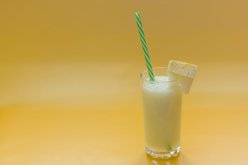 Melon smoothie in glass with piece of melon and straw on yellow background