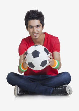 Portrait of young boy smiling while holding soccer ball over white background 