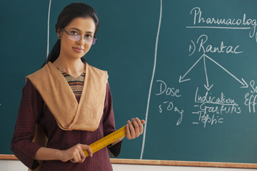 Portrait of young female teacher holding ruler against chalkboard 