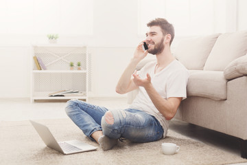 Smiling young man at home with laptop and mobile