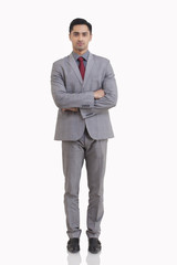 Full length portrait of young businessman with arms crossed standing against white background 