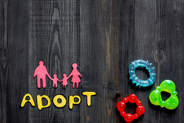 Adopt word, paper silhouette of family and toys on dark wooden table background top view copyspace